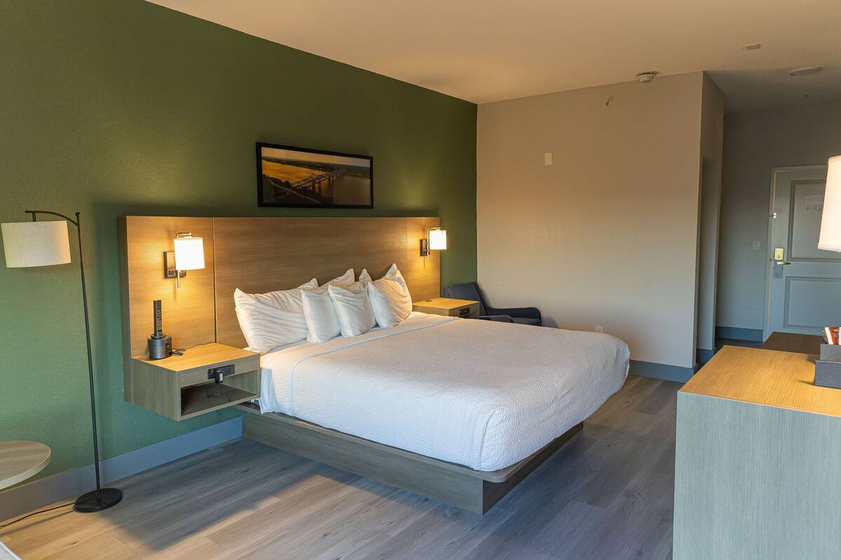 A hotel room with a bed, bedside tables, a nightstand, a desk, and a chair.
