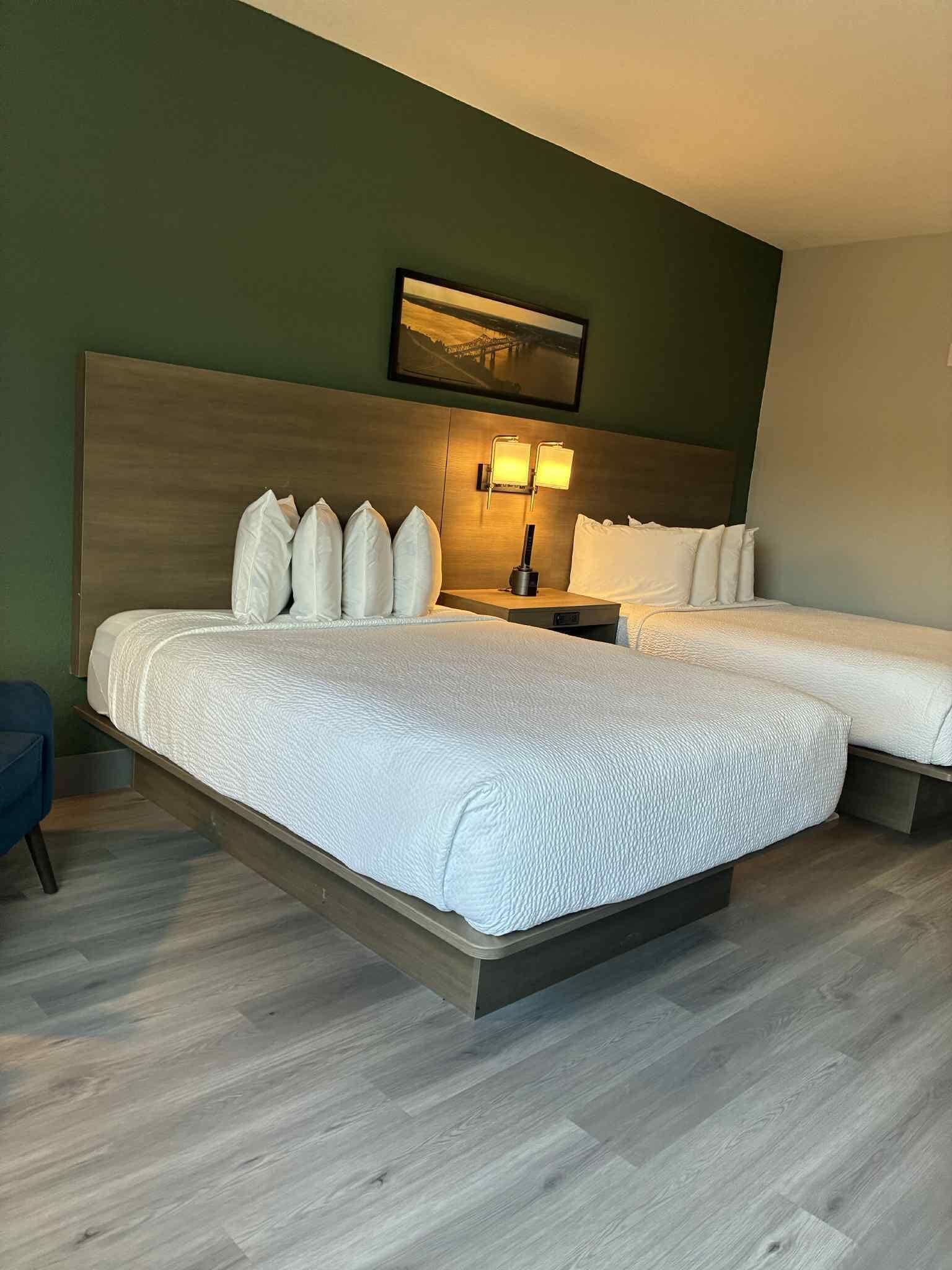A double bed with white bedding, a nightstand with a lamp, and a painting above the bed.