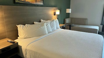 A hotel room with a large bed, a nightstand, a lamp, and a chair.