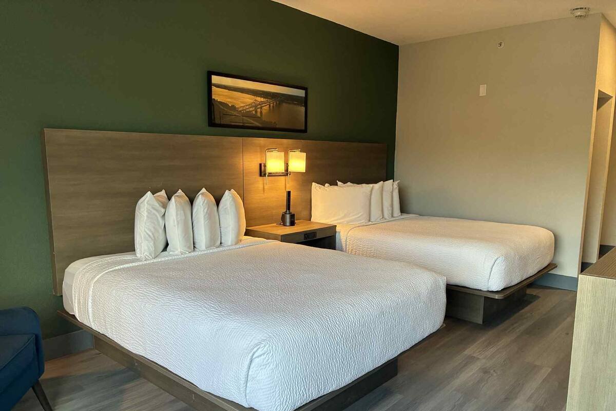 A hotel room with two beds, a nightstand, a lamp, and a framed picture on the wall.