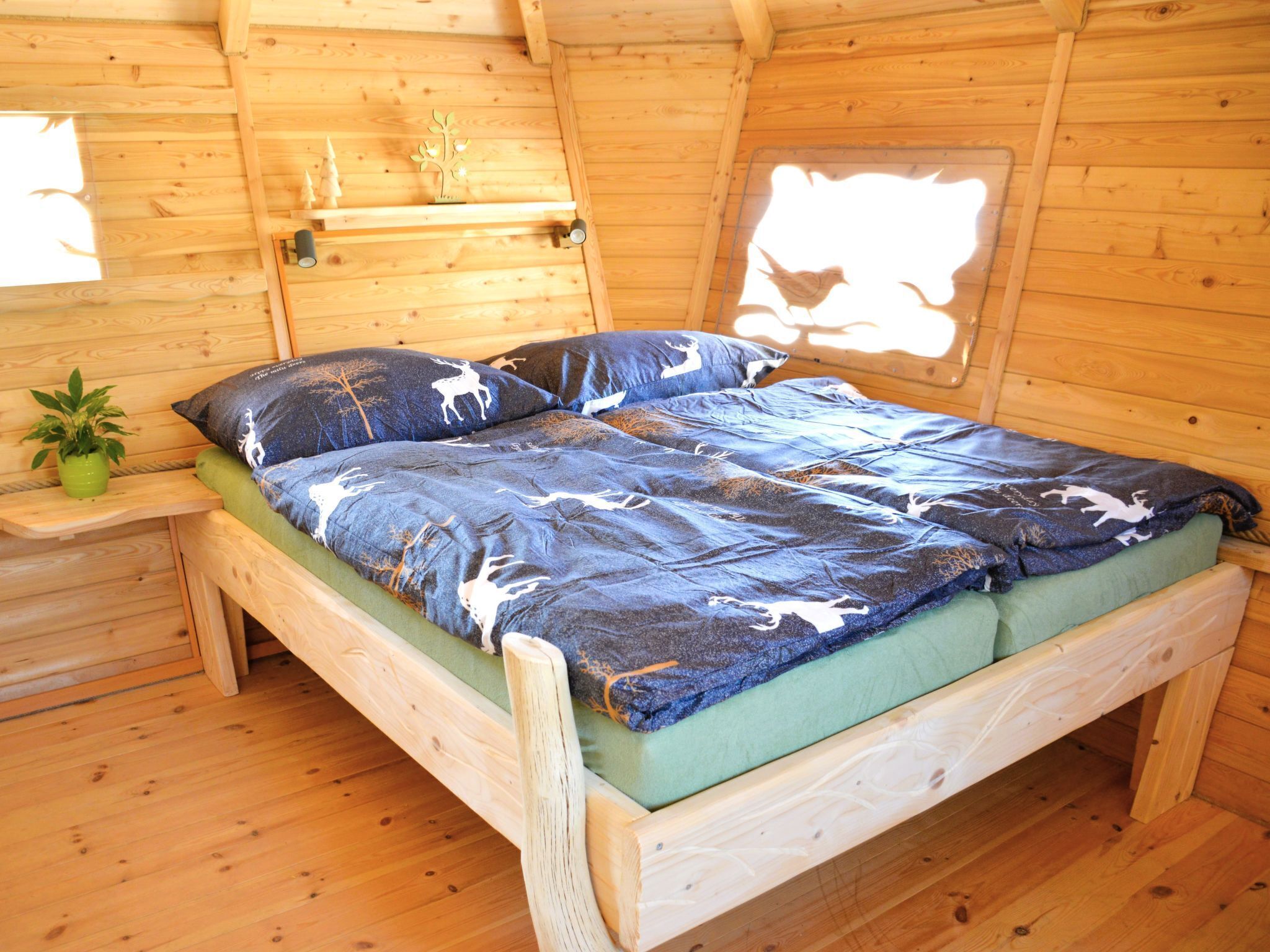 Un dormitorio de cabaña de madera con una cama, almohadas, una mesita de noche y una planta pequeña.