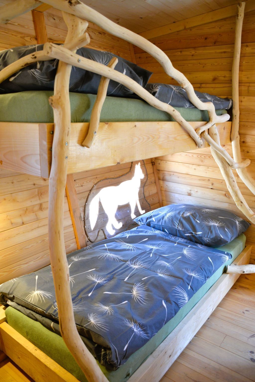 A bunk bed with a unique branch structure above the lower bunk, a green mattress, and a blue mattress with a dandelion pattern.