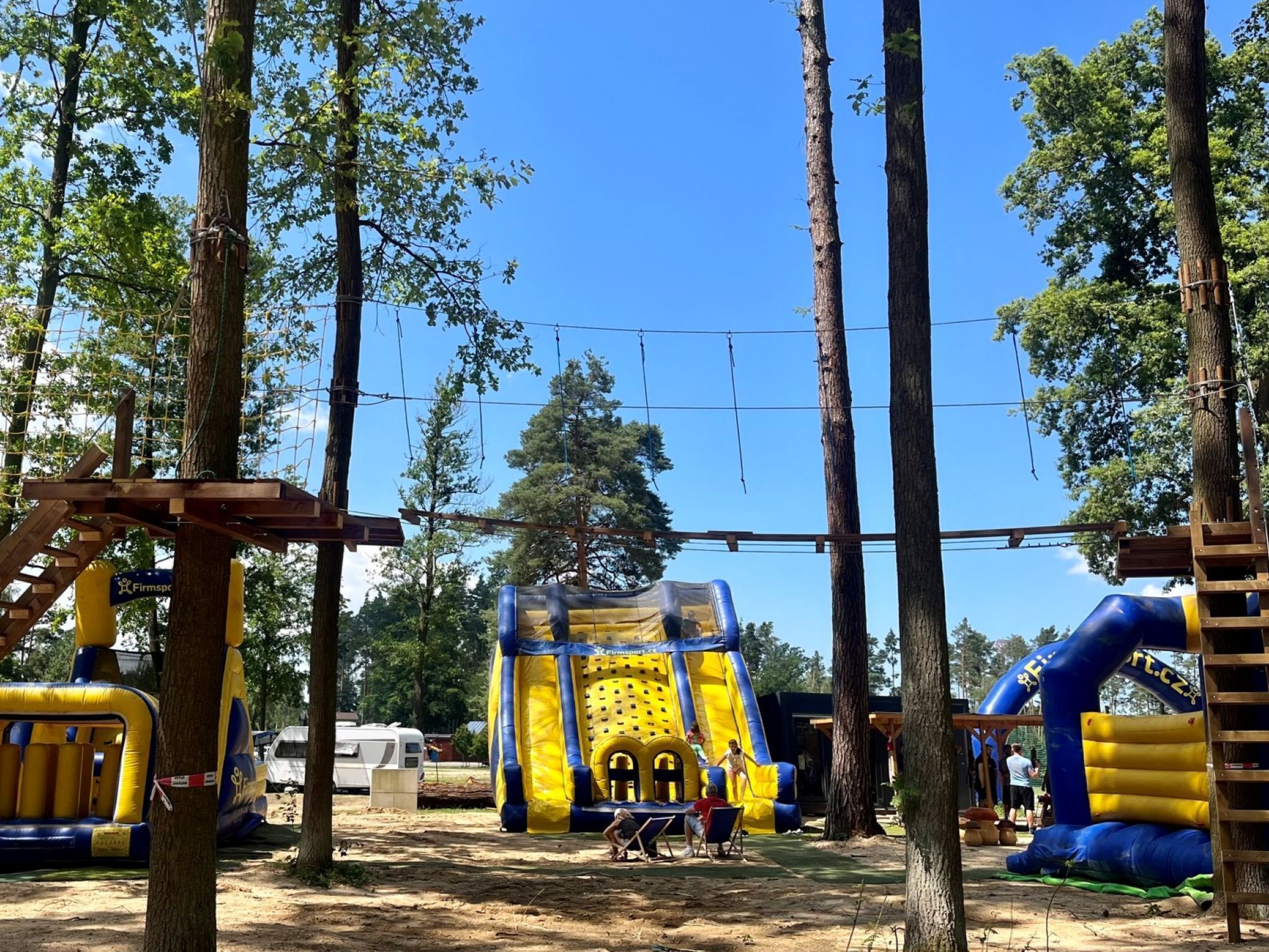 An outdoor playground with inflatable structures, including a slide and climbing net, surrounded by trees.