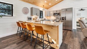A modern kitchen with a wooden ceiling, a central island with bar stools, and stainless steel appliances.