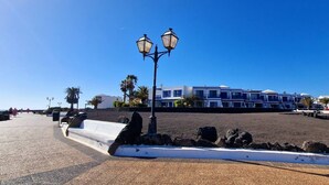 Un paseo marítimo con una hilera de edificios modernos frente al mar, un farol y un cielo azul despejado.