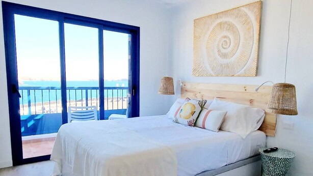 Un dormitorio con una cama grande, vista al mar a través de una puerta corrediza y cabecera de madera.