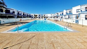 Una piscina rectangular con agua cristalina azul, rodeada por una solana con baldosas.