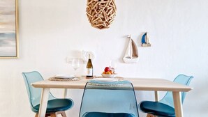 Un comedor con una mesa blanca, sillas azules, una lámpara colgante de fibra y un estante con una maqueta de un velero.
