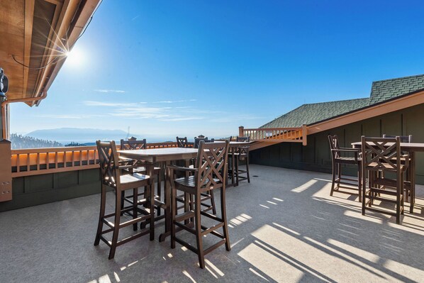 A rooftop terrace with wooden tables and chairs, a view of the mountains, and a clear sky. - Spacious 3 bedroom condo with incredible ski access / hot tub / gym / underground parking (Whitefish)