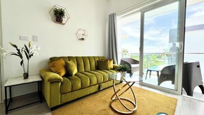 Una sala de estar moderna con un sofá verde, una mesa de centro de vidrio y vistas al exterior a través de puertas correderas grandes.