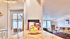A kitchen with a granite countertop, a bowl of fruit, and a microwave. There is a dining area with a couch and a colorful rug. - Sauzelle by Interhome (Ile d'Oléron)