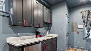 A modern kitchen with dark cabinets, a stainless steel refrigerator, and a marble countertop.