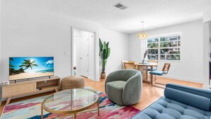 A modern living room with a television, sofa, round coffee table, and a dining area with a table and chairs.