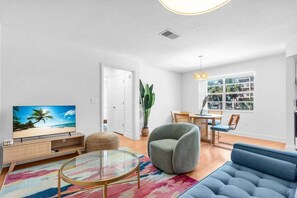 A modern living room with a television, sofa, round coffee table, and a dining area with chairs and a table.