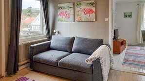 A living room with a grey sofa, two wall-mounted paintings of flamingos, a radiator, a TV on a wooden stand, and a colorful striped rug. - 3 bedroom amazing home in Dyrön (Dyrön)