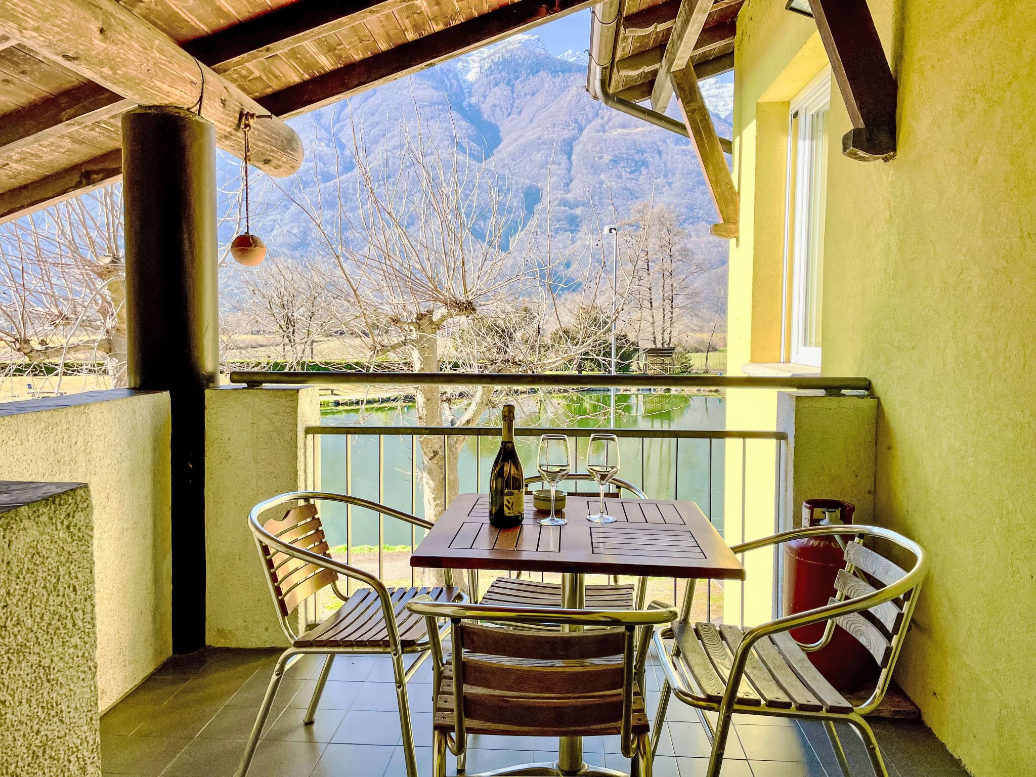 Um pátio com mesa e cadeiras, uma garrafa de vinho e vista para montanhas.