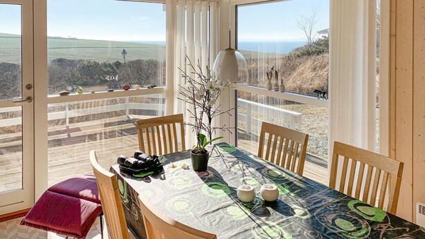 Un comedor con una mesa dispuesta para dos, un banco y vistas del paisaje a través de amplios ventanales.