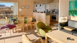 Una cocina moderna con armarios de madera, una zona de comedor con sillas de madera, un sillón verde y un sofá.