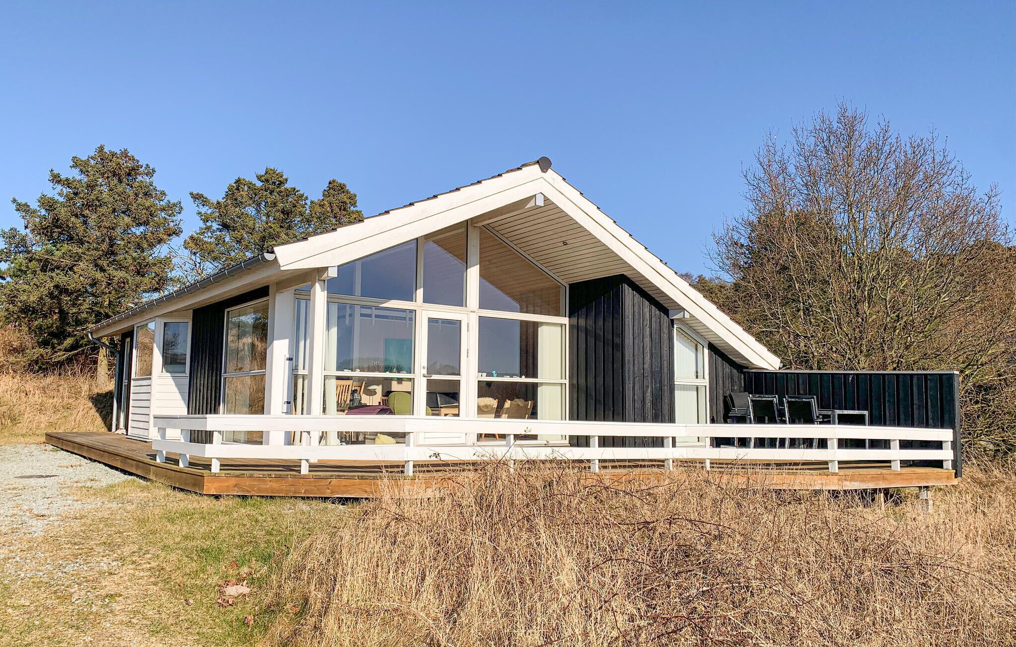 Een modern, gelijkvloers huis met grote ramen, een houten terras en een schuin dak.