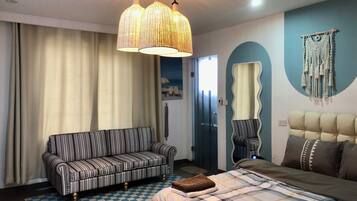 A hotel room with a striped sofa, a bed with a plaid bedspread, a checkered rug, a large mirror, and a macrame wall hanging.