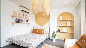 Une chambre moderne avec un lit, un canapé, une plante en pot et des étagères remplies de livres et d’objets décoratifs.