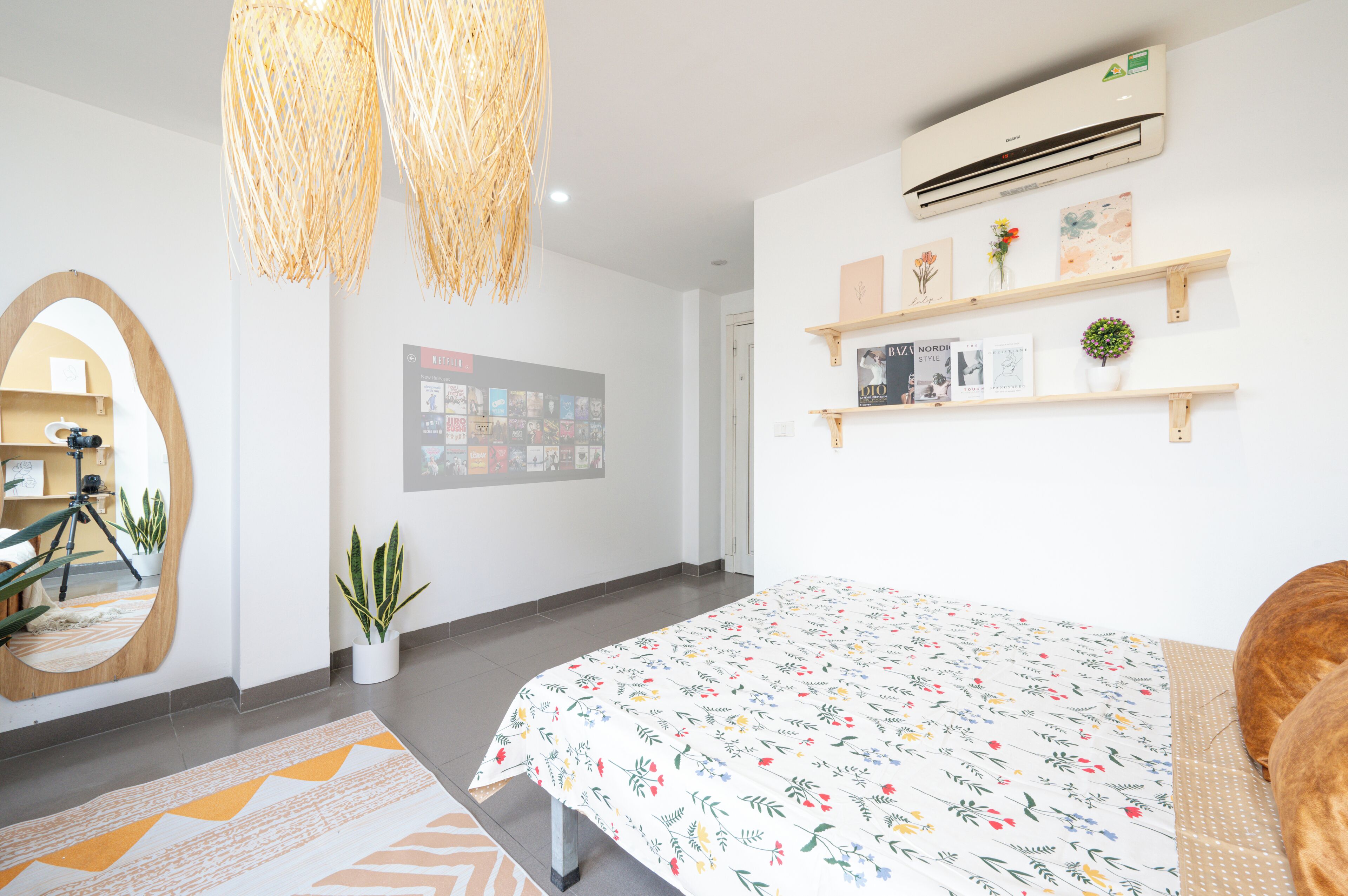 A modern bedroom with a large bed, a mirror, a wall-mounted air conditioner, and shelves with books and decorative items.