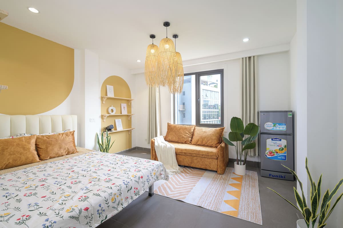 A modern hotel room with a bed, a sofa, a dining table, and a refrigerator.