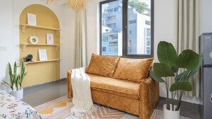 Un salon moderne avec un canapé, une grande fenêtre, une plante et une étagère décorative.