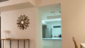 A modern living room with a wooden coffee table, a decorative mirror, and a view into the kitchen.