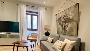 A modern living room with a grey sofa, a small round table, a television, and a large abstract painting on the wall.