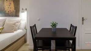 Et spiseområde med et mørkt træbord, to stole, en potteplante og en hvid væg med et ur.