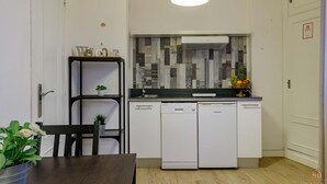 Et kompakt køkken med hvide skabe, en sort bordplade og en moderne pendel.