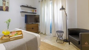 Ein Hotelzimmer mit Bett, Schreibtisch, Stuhl, Lampe und Frühstückswagen.