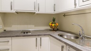 Eine Küche mit weißen Schränken, einer Granit-Arbeitsplatte, einer Edelstahl-Spüle und einer Obstschale mit Äpfeln, Orangen und einer Ananas.