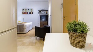 Ein Flur, der in einen Raum mit einem Bett, einem Sessel, einem Fernseher und einem an der Wand befestigten Regal führt.