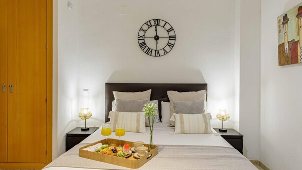 Ein Hotelzimmer mit Bett, einer Holztür, einer Wanduhr, Nachttischlampen und einem Tablett mit Frühstücksgegenständen.