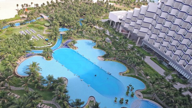 Een resort met meerdere zwembaden, palmbomen en een modern gebouw met balkons.