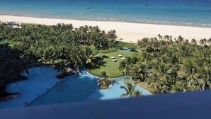 Een resort met een zwembad, palmbomen en uitzicht op het strand.