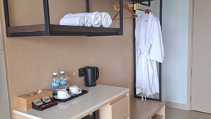 Een compacte hotelkamer met een stapelbed, een kitchenette, een klein zithoekje en een badjas hangend aan een rek.