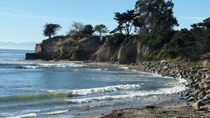 Uma praia rochosa com ondas, árvores e céu claro.