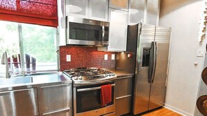 Une cuisine moderne dotée d’appareils électroménagers en acier inoxydable, d’un plan de travail rouge en carreaux et d’un revêtement de sol en bois.