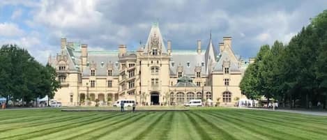 A large, historic building with a symmetrical facade, multiple towers, and a well-maintained lawn in front.