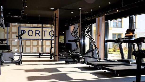 Un gimnasio con diverso equipo de ejercicio, una caminadora y una pared con la palabra 'PORTO' a la vista.