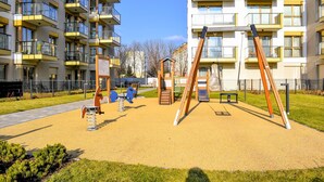 Un parque infantil con columpios y toboganes, rodeado de edificios de apartamentos.