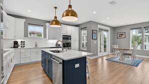 A modern kitchen with white cabinets, a central island, stainless steel appliances, and pendant lighting. - Storybook - Near Beach with Private Pool (Destin)