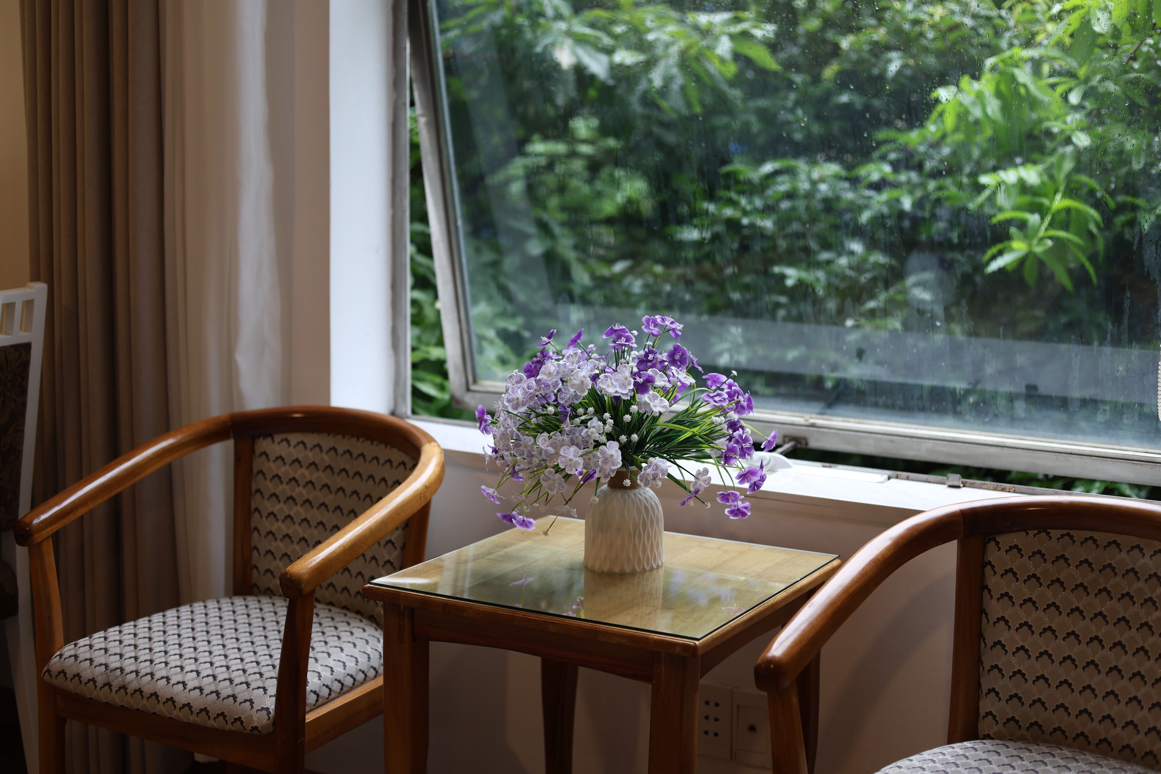 Een kamer met een houten stoel en een kleine tafel met een bloemenvaas.