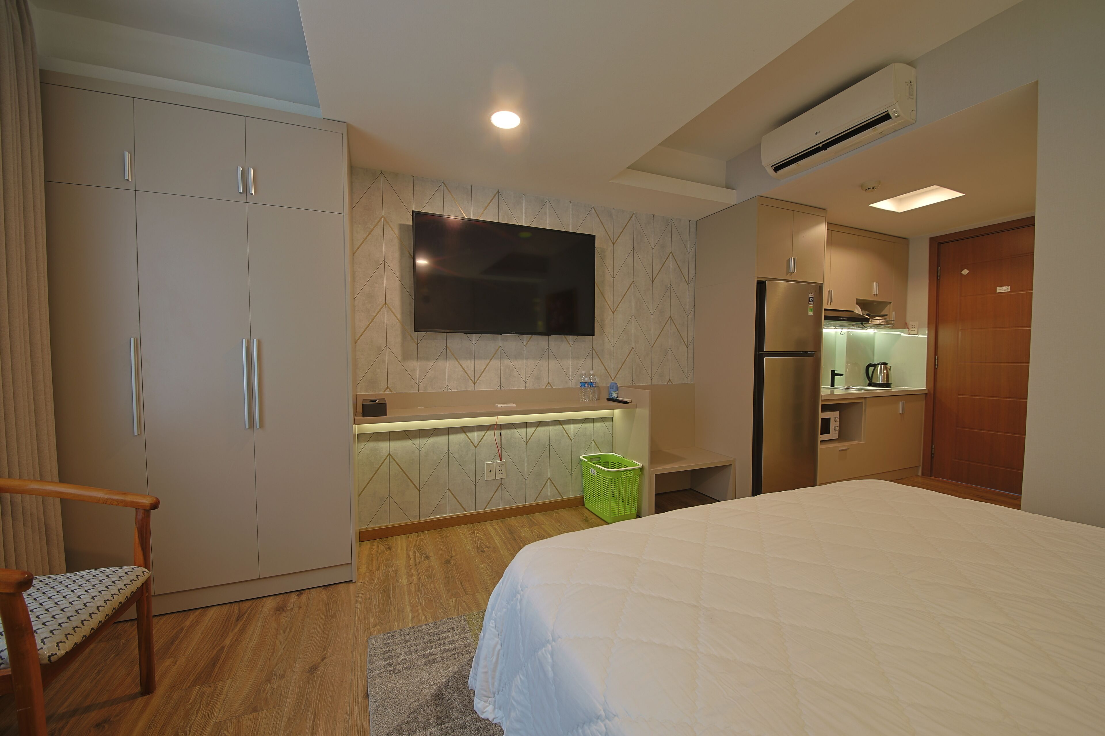 A hotel room with a bed, wardrobe, TV, kitchenette, and a chair.