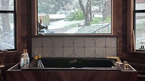A wooden interior with a kitchen area featuring a built-in sink, a window with a view of a snowy landscape, and a ceiling with hanging light fixtures. - Charming Rustic Mountain Cabin, Near Yosemite,Amazing Views, and a Fireplace (Wishon)