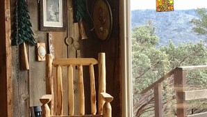 A rustic wooden chair with a cushion in a room with wooden walls, a window with a view of trees, and a hanging light fixture. - Charming Rustic Mountain Cabin, Near Yosemite,Amazing Views, and a Fireplace (Wishon)