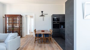 A dining area with a wooden table and chairs, a cabinet with glass doors, and a modern kitchen with dark cabinetry.